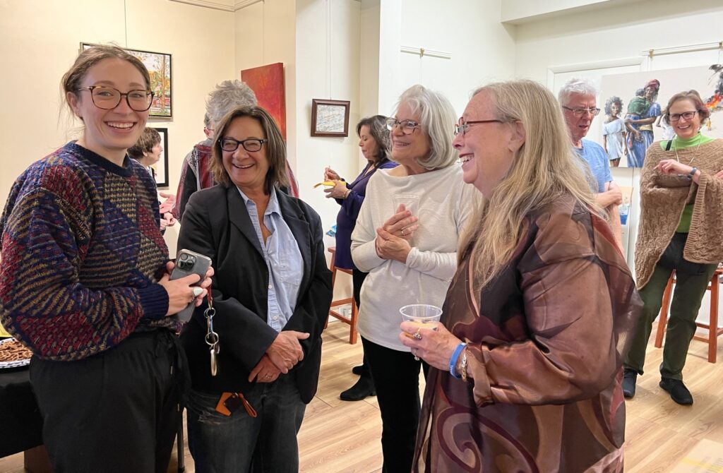 Guests of all ages chatting and smiling at an artist reception, with artwork on the walls